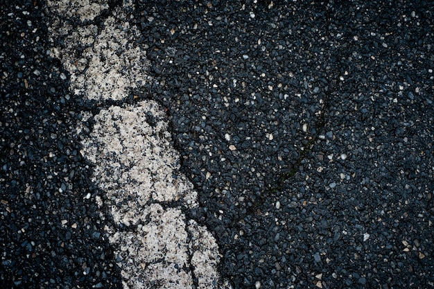 Viejo asfalto negro con franja blanca y fondo de grietas