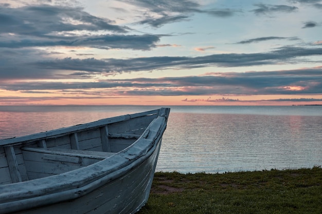 Un viejo barco de madera pintado de blanco en la orilla de una hermosa bahía con un cielo nublado de colores bajo los rayos del sol del amanecer