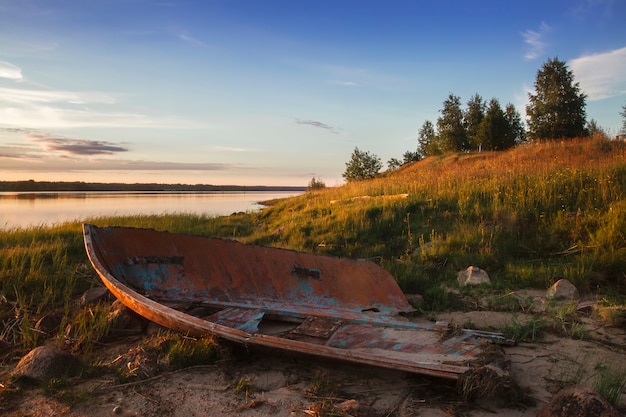 Viejo barco roto en la orilla del lago al atardecer