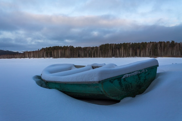 Un viejo barco verde en un lago congelado. Barco cubierto de nieve pura