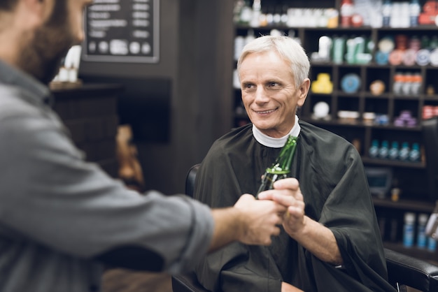 Viejo bebe alcohol en la silla de barbero en la barbería,