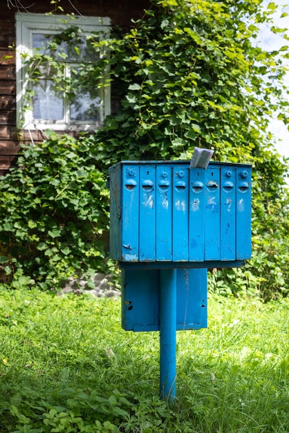 Un viejo buzón de hierro azul para correo y correspondencia en un pueblo cerca de una casa cubierta de vegetación