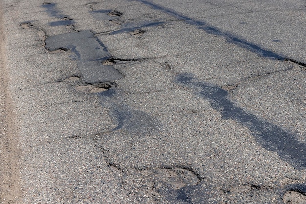 Un viejo camino pavimentado con muchos agujeros y daños muy mala calidad de la carretera con asfalto dañado de mala calidad