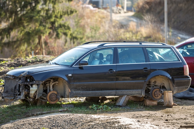 Viejo coche de basura roto oxidado abandonado después de accidente de accidente sin ruedas en sellos de madera cubiertos de nieve en día de invierno al aire libre abandonado en el campo