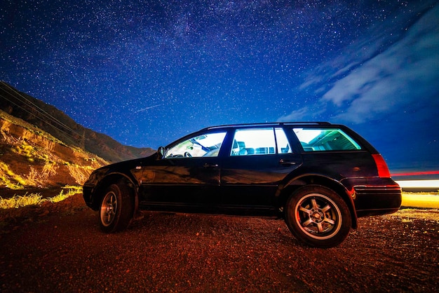 Viejo coche negro en una noche de verano estrellada en el desierto