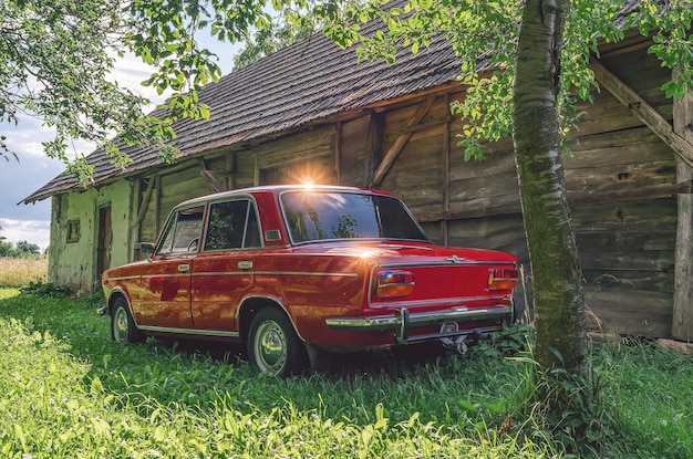 Viejo coche rojo brillante en el fondo de un cobertizo de madera abandonado Viejo coche Zhiguli soviético rojo Bengalas solares