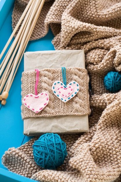 Foto viejo cuaderno con tapa de punto con corazón de fieltro junto a la brillante maraña de hilo de tejer y manta de punto sobre fondo azul.