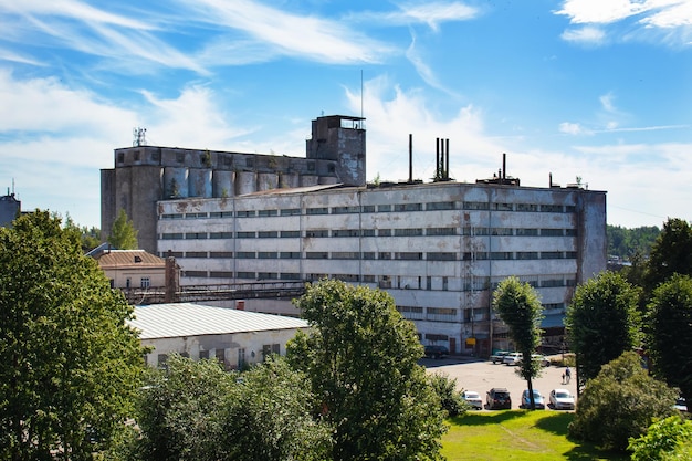 Viejo elevador de granos y edificio gris entre árboles verdes bajo el cielo azul Vyborg Rusia Agosto 2022