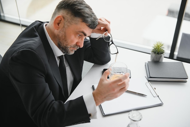 Viejo empleado bebiendo alcohol en el lugar de trabajo