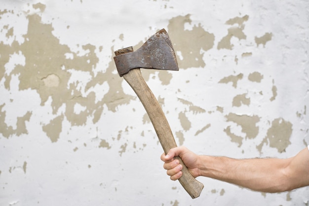 Viejo hacha oxidada en la mano del hombre contra la pared destartalada