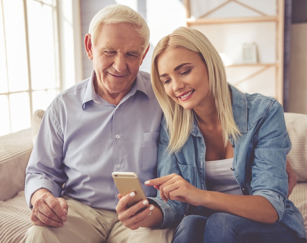 El viejo y la hermosa joven están usando un teléfono inteligente.