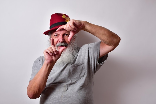 Viejo hombre americano con una camisa gris y un sombrero de fieltro rojo haciendo un cartel con las manos