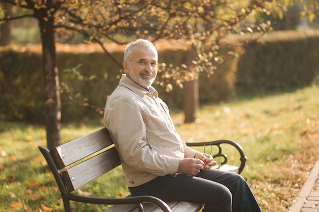 Viejo hombre canoso descansa en el banco en el parque de otoño
