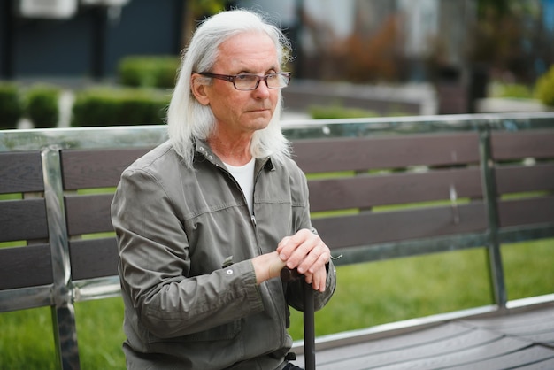 Viejo hombre canoso descansa en el banco en el parque de verano