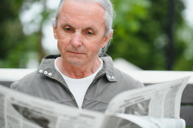 Viejo hombre canoso descansa en el banco en el parque de verano