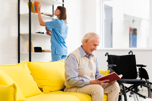 Viejo hombre leyendo un libro mientras está sentado en el sofá amarillo