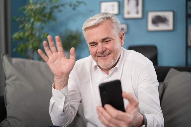 Viejo hombre de mediana edad que tiene chat de video usando un teléfono inteligente chateando con su hijo en la pantalla del teléfono móvil sonriendo