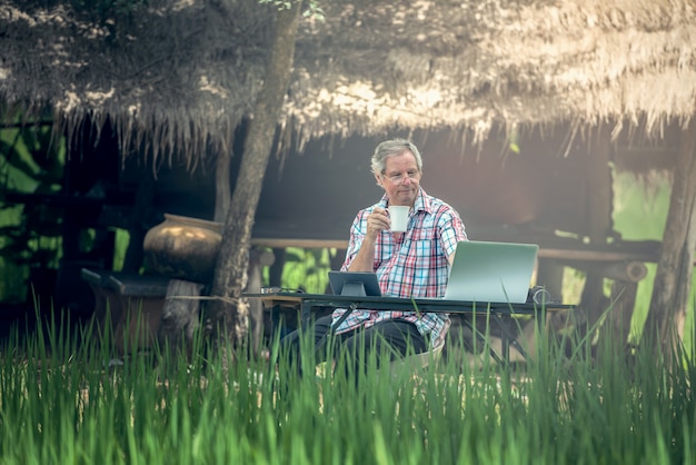Viejo hombre que se sienta en un escritorio en un al aire libre usando una computadora portátil