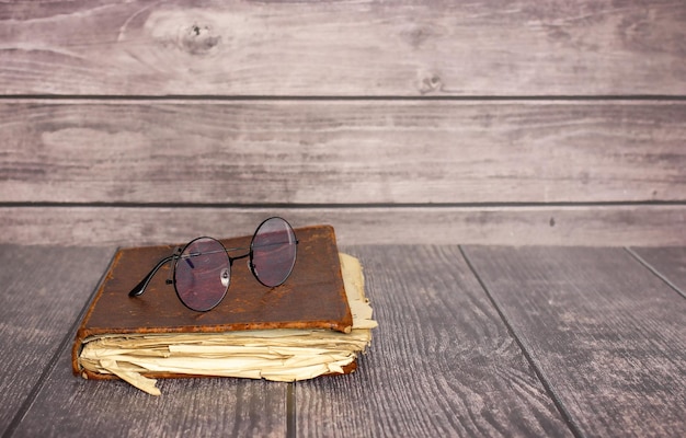 Viejo libro cerrado en mal estado con gafas sobre una mesa de madera. Vista superior, copie el espacio.