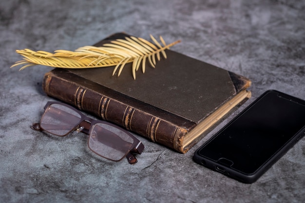 Un viejo libro con una hoja de palma amarilla y vasos sobre una mesa gris.