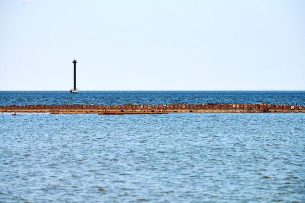 Viejo muelle de mar oxidado abandonado para amarrar barcos y yates en el fondo de la superficie del agua de mar azul en calma y cielo despejado, espacio de copia. Oceanside, mar en colores vibrantes y horizonte espectacular