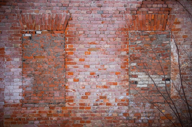 Viejo muro de ladrillo rojo en mal estado con ventanas tapiadas