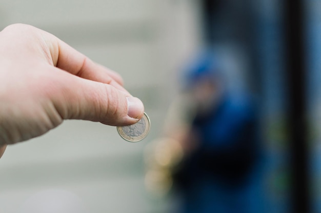 El viejo músico de la calle toca el saxofón con una moneda borrosa en la mano enfocada