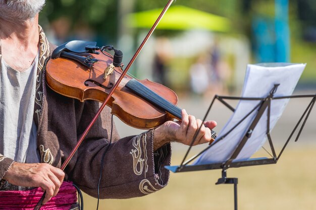 Viejo músico con un violín cerca de un atril en la calle_