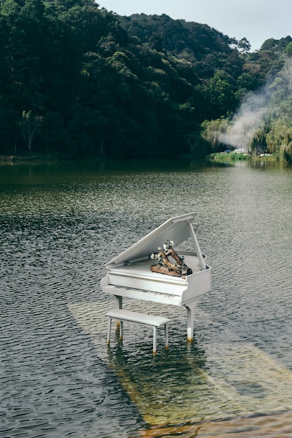 Viejo piano oxidado blanco dentro del lago contra el bosque de pinos en Da Lat