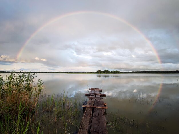 Viejo puente de madera en el lago en el fondo de un hermoso arco iris en un cielo nublado paisajes de