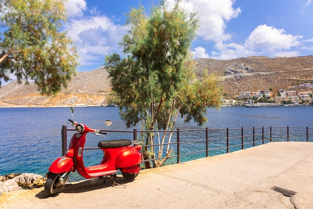 Viejo scooter rojo está estacionado en el paseo marítimo de la hermosa isla de Symi Colorido paisaje de verano