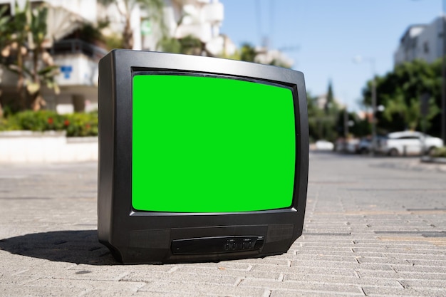 Viejo televisor con una pantalla verde en la calle de la ciudad con coches