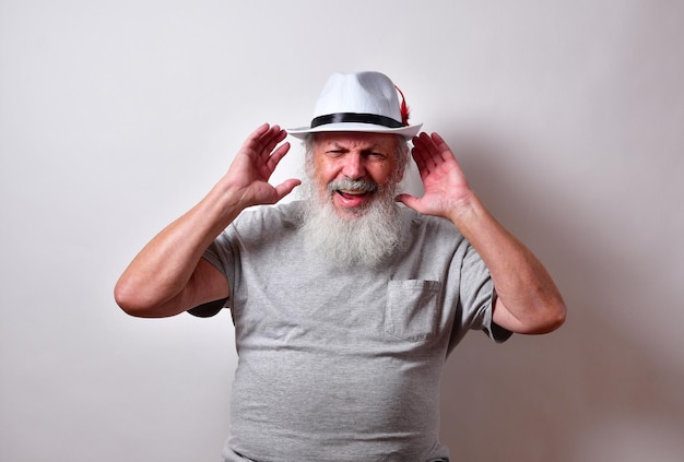 Viejo varón americano con una larga barba blanca tapándose las orejas para oír mejor