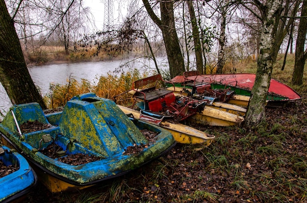 Viejos barcos y catamaranes se oxidan al aire libre Vertedero en el bosque al pie de la orilla del río de equipos de agua obsoletos Cerca crecen grandes abedules y otros árboles Contaminación ambiental