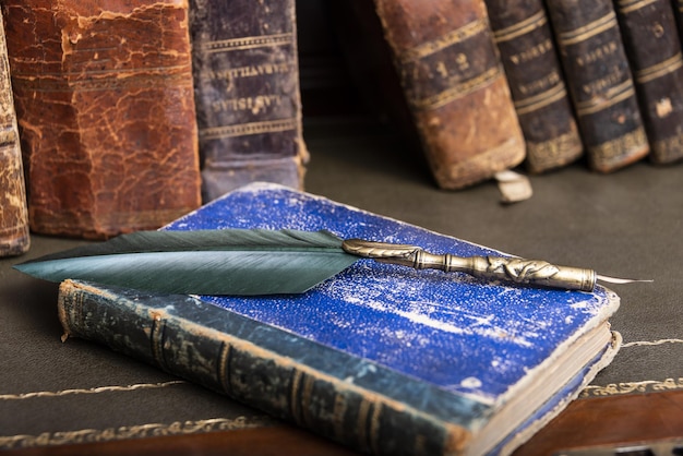 Viejos libros de pluma y tintero vintage en el escritorio de madera en la antigua oficina contra el fondo de la librería y los rayos de luz Antecedentes conceptuales sobre temas de literatura de educación histórica