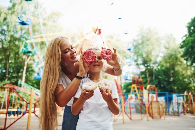 Viel Spaß mit Donuts. Fröhliches kleines Mädchen, ihre Mutter, haben eine gute Zeit im Park zusammen in der Nähe von Attraktionen.