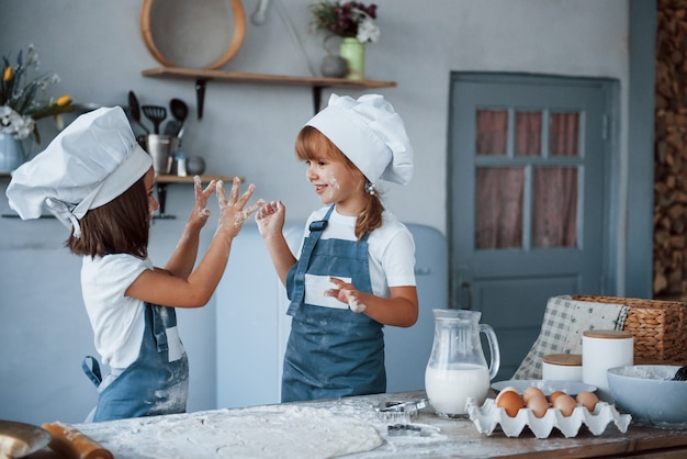 Viel Spaß während des Prozesses. Familienkinder in weißer Kochuniform, die Essen in der Küche zubereiten.