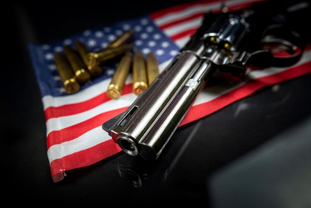 Viele gelbe Kugeln und eine Revolverpistole auf der Flagge der Vereinigten Staaten isoliert auf schwarzem Tisch