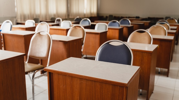 Viele Holztische und -stühle, die im Klassenzimmer der Universität gut angeordnet sind, aber kein Student. Leeres Klassenzimmer ohne Schüler, da die Schule während der COVID-19-Pandemie gesperrt ist.
