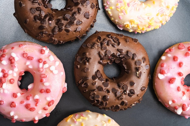 Viele kleine Donuts mit weißem Rosa und Schokoladenglasur auf einer schwarzen Platte von oben