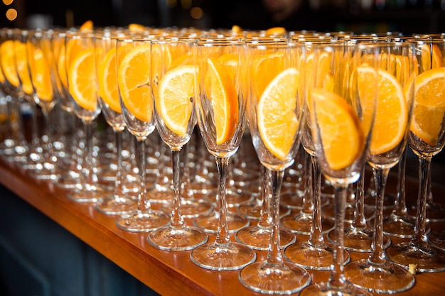 Viele leere Gläser stehen auf dem Glas, im Glas liegt eine Orangenscheibe. Gläser stehen auf einem Holztisch.