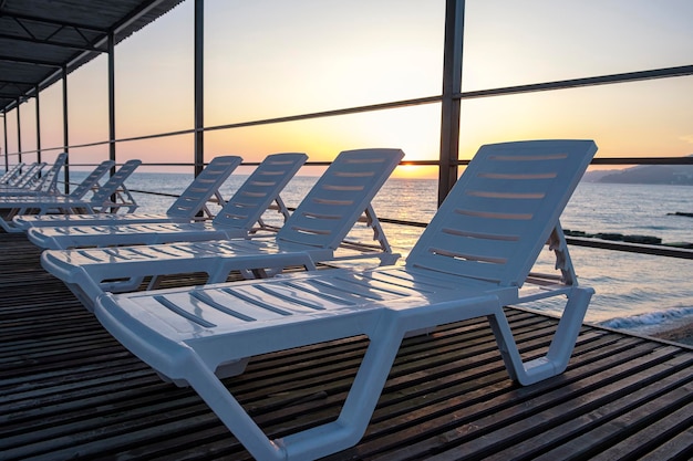 Viele leere weiße Liegen in Reihe im luxuriösen tropischen Resorthotel Blick auf das Meer und den Sonnenuntergang vom hohen Pier Sommerferien und Urlaubsreise- und Tourismuskonzept