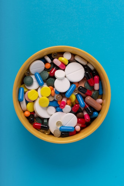 Viele medizinische Pillen und Kapseln in einer Schüssel auf blauem Hintergrund, Ansicht von oben