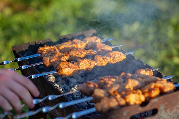 Viele saftige Fleischspieße hintereinander auf dem Grill. Fleischstücke auf Metallspieße auf dem Grill bei Sonnenuntergang aufgereiht. Der Prozess des Kochens von Kebabs mit viel Rauch. Kochen in der Natur