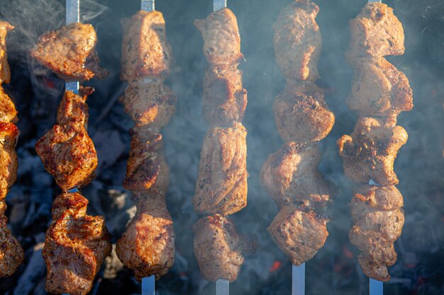 Viele saftige Fleischspieße hintereinander auf dem Grill. Fleischstücke auf Metallspieße auf dem Grill bei Sonnenuntergang aufgereiht. Der Prozess des Kochens von Kebabs mit viel Rauch. Kochen in der Natur