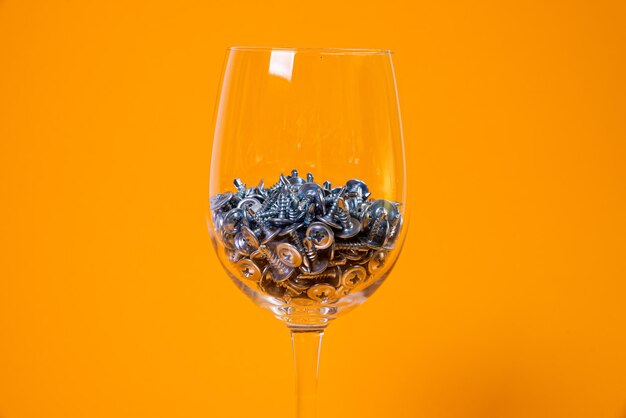 Viele selbstschneidende Metallschrauben aus Stahl in einem Glas im Eimer selbstschneidende Schraube für Metall für Eisen verchromte selbstschneidende Schraube auf orangegelbem Hintergrund