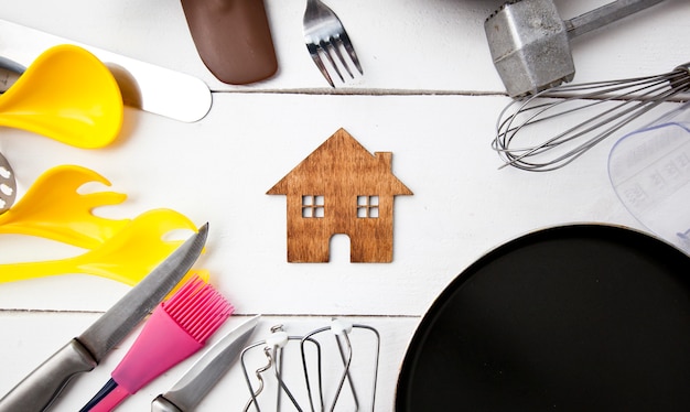 Viele verschiedene Küchenutensilien auf Holztisch und ein kleines Holzhaus dazwischen