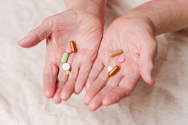 Viele verschiedene Pillen in den Händen einer älteren Person.