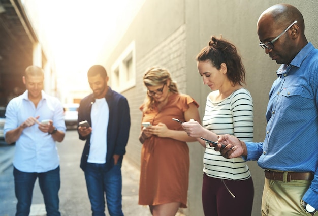 Vielfältige Gruppe erwachsener Menschen, die sich außerhalb des Büros verbinden und soziale Netzwerke aufbauen Geschäftsleute, die in einer Arbeitspause außerhalb des Büros eine SMS schreiben, surfen und Informationen auf Telefonen online austauschen