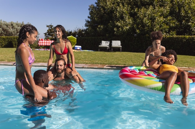 Vielfältige Gruppe von Freunden, die Spaß haben und im Schwimmbad auf Schultern herumtragen. Im Sommer draußen abhängen und entspannen.